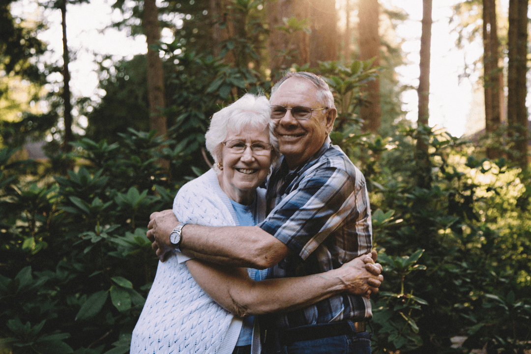 An elderly couple embraces while smiling