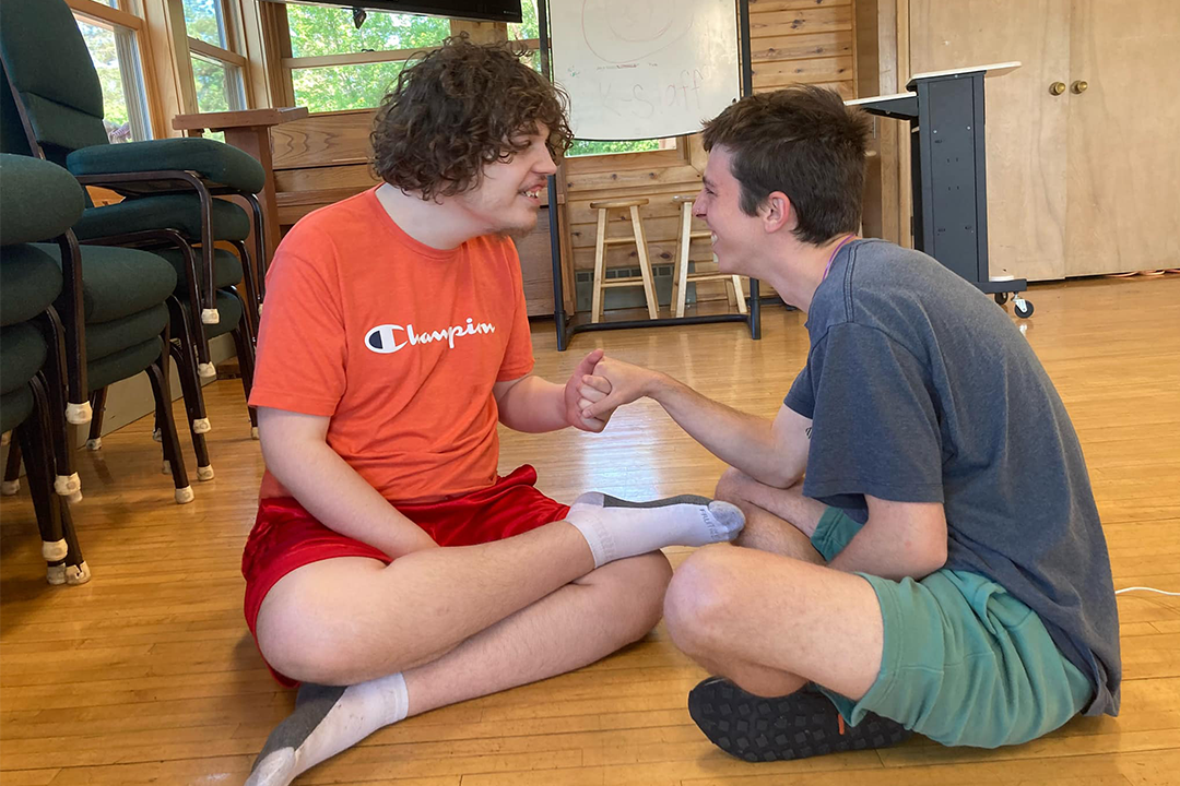 Two young men sit on the floor together, clearly having a great time