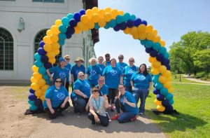 The AuSM staff wearing matching blue tshirts stand under a balloon arch