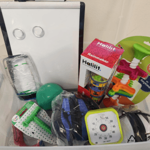 An AuSM Sensory Kit: a bin filled with a white board, fidgets, a time timer, and other tools