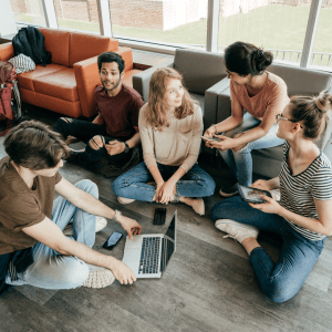 A group of young adults sits on chairs and the floor, chatting together