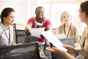 A group of professionals sits in a circle holding papers and discussing something intently