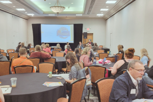 A long view of a breakout session room at the 2023 Minnesota Autism Conference, with attendees sitting at circular tables