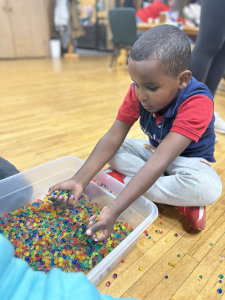 A young boy sits on the floor and buries his hands in sensory beads, looking transfixed