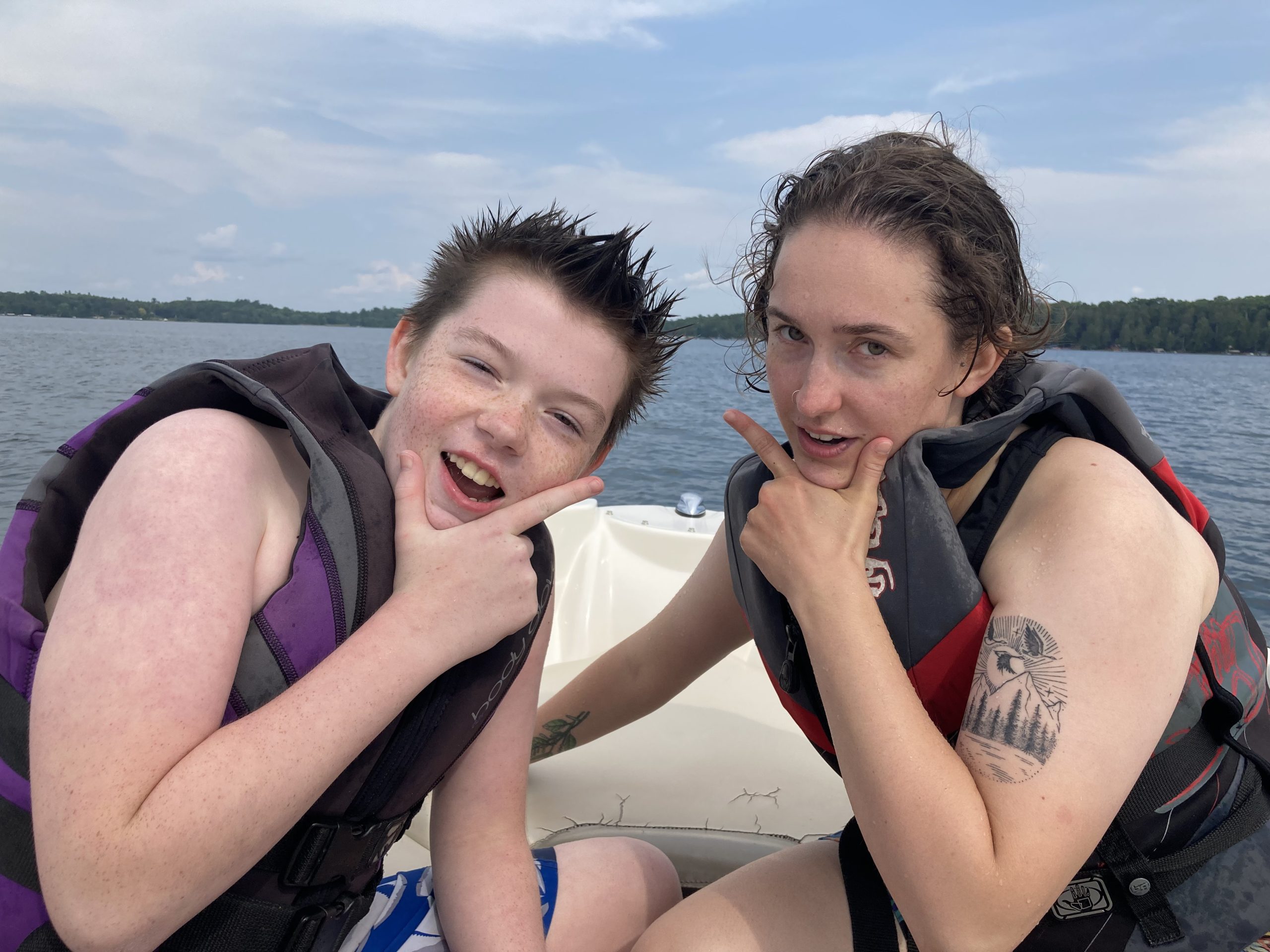 A camper and his counselor sit on a boat wearing life vests and ham it up for the camera