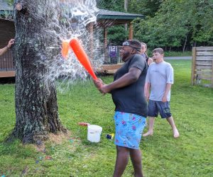 A young man breaks open a water balloon with a plastic baseball bat