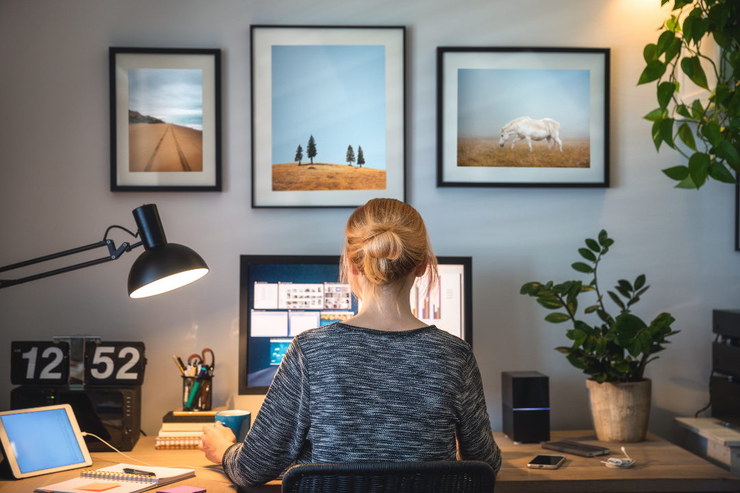 A woman sits at a home office in front of al beautifully organized desk. Her back is to us and she's working at a computer.