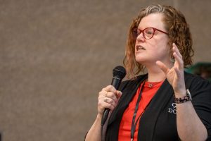 A speaker at the 2024 Minnesota Autism Conference holds a microphone and gestures with one hand while presenting.