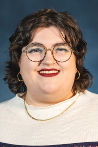 Headshot of Mason Esposito, a nonbinary person with short, dark, curly hair, glasses, and hoop earrings