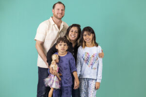A family of four with disabilities stands in front of a teal background